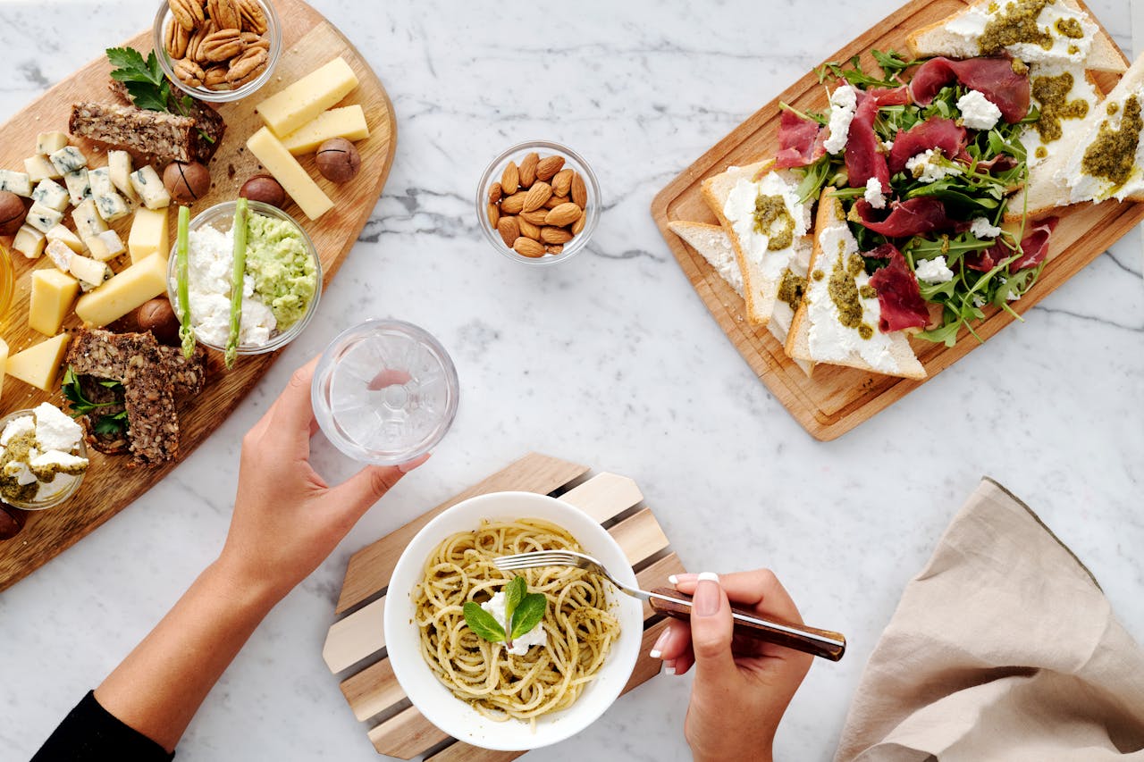 Delicious flat lay of gourmet cheese board, pasta, and appetizers on marble table.